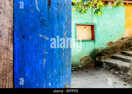 Rustic open blue painted door & turquoise & yellow building wall with boarded up window in Guatemala, Central America Stock Photo