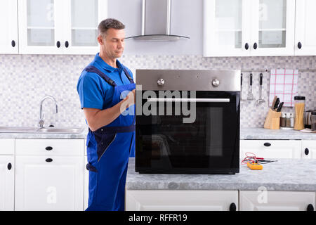 Mature Male Technician Repairing Oven On Kitchen Worktop Stock Photo