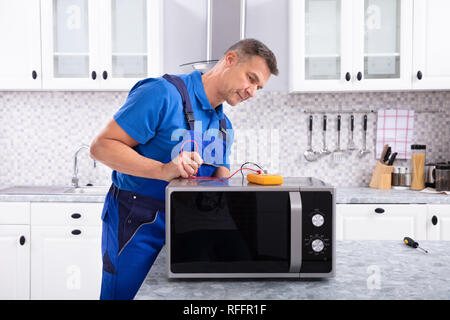 Male Handyman Repairing Microwave Using Digital Multimeter In Kitchen Stock Photo