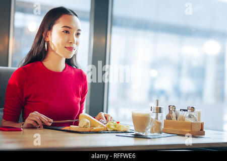 Woman feeling relieved while enjoying breakfast in cafeteria Stock Photo