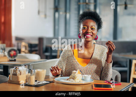 Cheerful woman enjoying yummy dessert and latte in cafeteria Stock Photo