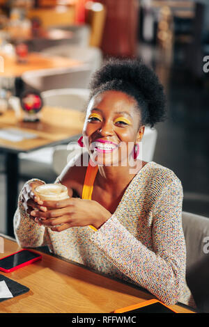 Dark-haired woman smiling broadly while enjoying coffee break Stock Photo