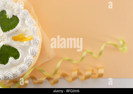 White cream cake with green hearts on a peach background with green and orange ribbon shot from above Stock Photo