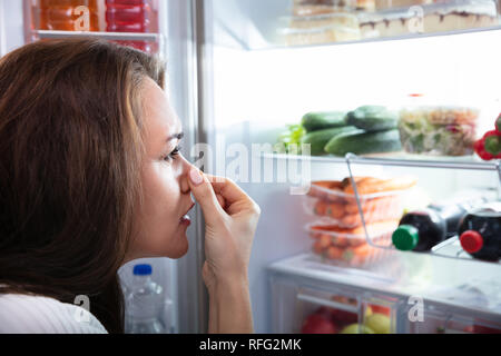 Side View Of Young Woman Recognizing Bad Smell Coming From The Refrigerator Stock Photo