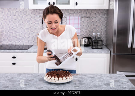 Portrait Of A Smiling Young Woman Grating Chocolate Over Cake Stock Photo