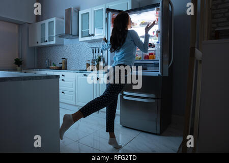 Woman Opening Refrigerator Door With Various Food In Kitchen Stock Photo