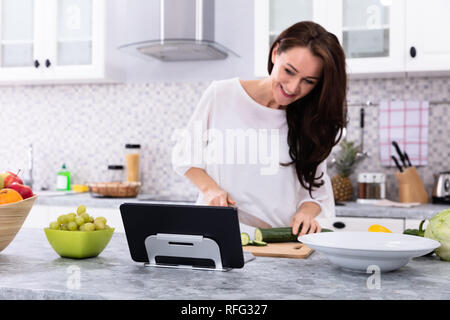 Happy Young Woman Using Digital Tablet While Cooking Food In Kitchen Stock Photo