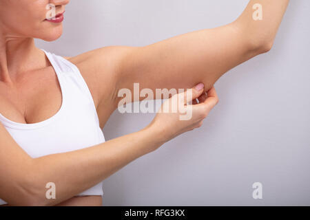 Close-up Of A Woman Checking Excessive Fat On Her Arms Over Grey Background Stock Photo