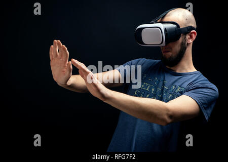 Male using VR gear is dodging with both hands. Shot in studio against black background Stock Photo