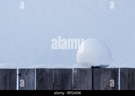 A beautiful clump of snow on a wooden fence with a snowy background. Christmas texture. Stock Photo