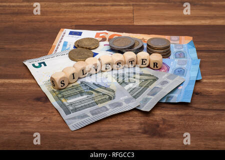 Die Euro Geldscheine und Münzen liegen auf dem Tisch mit dem Wort Silvester Stock Photo