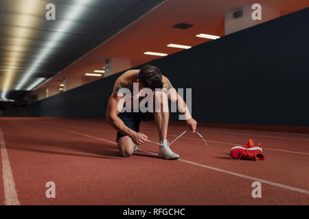 Very fit man on a an indoor track preparing to run by chaning his shoes and tying his laces Stock Photo