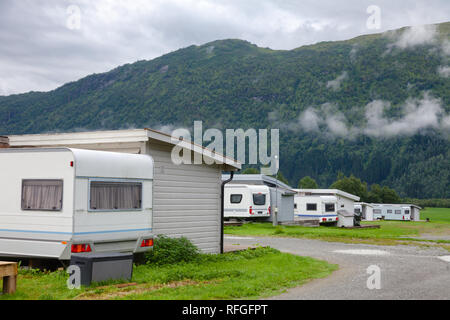 Grey wooden cabins with parked camper trailers at a campsite in Norway, Scandinavia. Cloudy moutain is seen in background Stock Photo