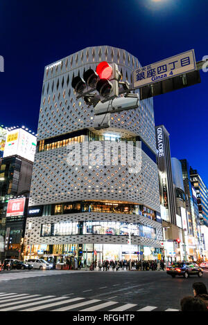 The white Ginza Place building and its aluminium panel façade. Night time, street crossing in foreground with Ginza 4 sign and red stop light. Traffic. Stock Photo
