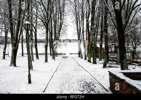 Beautiful park with old lamps, benches and lake with snow in winter Stock Photo