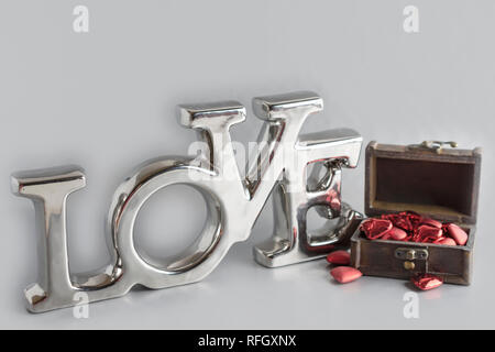 The word 'Love' with a chest of hearts.  'Love' is a chrome shiny decoration.  Chest lid open.  On a very light gray background. Stock Photo