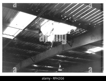 Black and white photograph, showing an interior shot of a military building, with a hole in its corrugated metal roof, photographed during the Vietnam War, 1968. ()