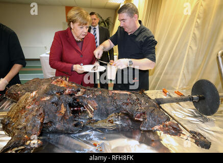 Trinwillershagen, Germany. 25th Jan, 2019. Angela Merkel (CDU, M), Chancellor of the Federal Republic of Germany, is given a piece of roast wild boar by Andre Teuerung, butcher, at the traditional New Year's reception of the district of Vorpommern-Rügen. Merkel represents the constituency with a direct mandate in the Bundestag. Credit: Bernd Wüstneck/dpa/Alamy Live News Stock Photo