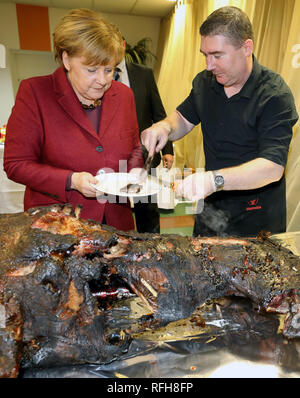 Trinwillershagen, Germany. 25th Jan, 2019. Angela Merkel (CDU), Chancellor of the Federal Republic of Germany, is having Andre Teuerung, butcher, give her a piece of roast wild boar at the traditional New Year's reception of the district of Vorpommern-Rügen. Merkel represents the constituency with a direct mandate in the Bundestag. Credit: Bernd Wüstneck/dpa/Alamy Live News Stock Photo