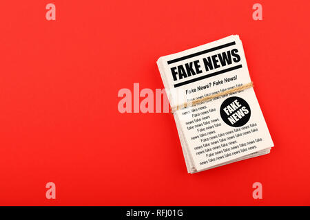 Close up stack of FAKE NEWS newspapers over red paper background with copy space, elevated top view, directly above Stock Photo