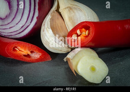 Close up one fresh red hot chili pepper onion and garlic cut to slices on background of black slate board, low angle side view Stock Photo