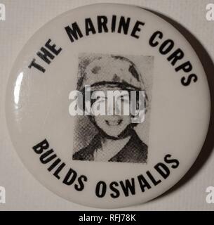 Black and white anti-war pin or button with a headshot of President John F Kennedy's assassinator, Lee Harvey Oswald, wearing a helmet and uniform, and smiling at the camera, during his posting with the United States Marine Corps, encircled by the text 'The Marine Corps Builds Oswalds', issued during the Vietnam War, 1965. ()
