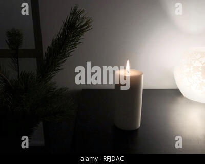 Burning white candle on black table with green fir tree and flower ornament lamp Stock Photo