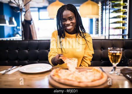 Young african girl in yellow sweater eating pizza at restaurant. Stock Photo