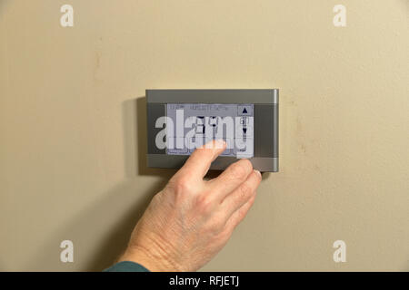 Hand adjusting temperature on digital programmable thermostat Stock Photo