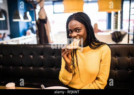 Young african american woman eating pizza in cafe Stock Photo