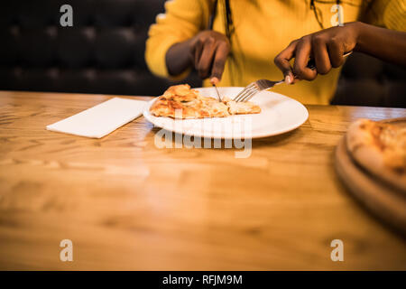 Young afro american woman wearing in yellow sweater eating pizza in cafe Stock Photo