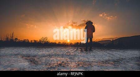 Young man standing in winter frozen nature and watching to the calm winter misty sunrise. Original wallpaper or background from nature