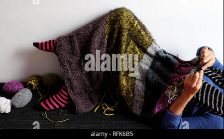 Asian woman lying on floor of home to knit woolen blanket for warm in wintertime, knitting is hobby in leisure activity to make handmade gift, photo o Stock Photo