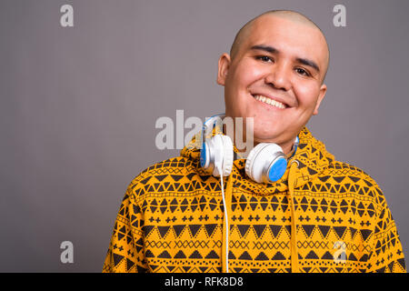 Young bald Asian man wearing headphones against gray background Stock Photo