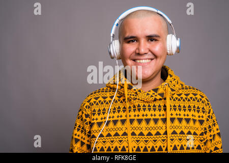 Young bald Asian man listening to music against gray background Stock Photo