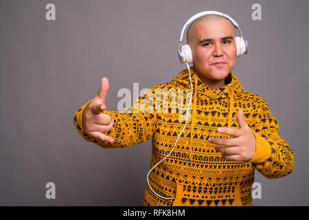 Young bald Asian man listening to music against gray background Stock Photo
