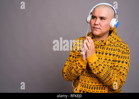 Young bald Asian man listening to music against gray background Stock Photo