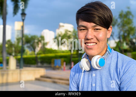 Young Asian teenage boy wearing headphones while relaxing at the Stock Photo