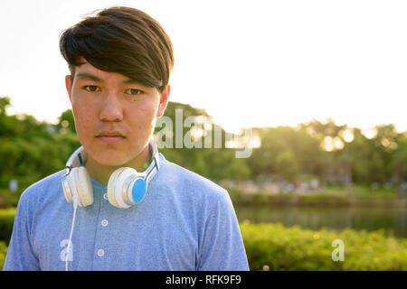 Young Asian teenage boy wearing headphones while relaxing at the Stock Photo