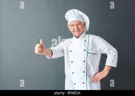 Senior chef studio standing isolated on gray showing thumb up looking camera friendly Stock Photo