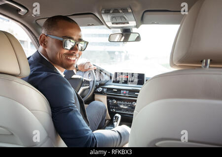 Young businessman driver in sunglasses sitting inside car looking back at camera joyful back seat view Stock Photo