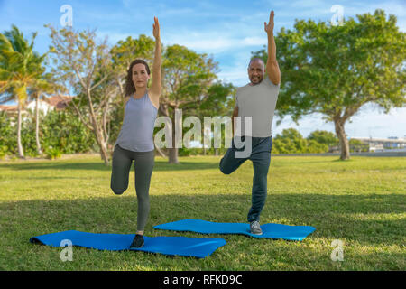They start by standing on one leg holding the other back and reaching up high with the other hand to balance themselves on yoga mats exercising. Stock Photo