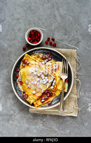Delicious crepes topped with pomegranate and sugar on plate flat lay.