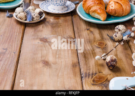 Easter breakfast flat lay with fresh coffee, berries and pastries , orange tulips, croissants with bacon and various sweets , colored quail eggs and s Stock Photo