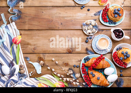 Easter breakfast flat lay with fresh coffee, berries and pastries , orange tulips, croissants with bacon and various sweets , colored quail eggs and s Stock Photo