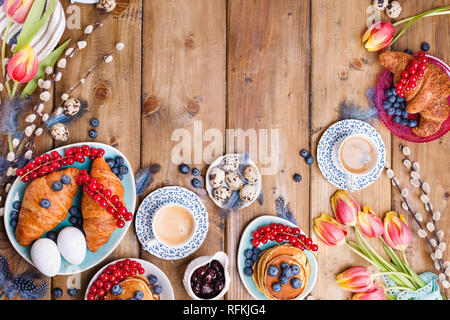 Easter breakfast flat lay with fresh coffee, berries and pastries , orange tulips, croissants with bacon and various sweets , colored quail eggs and s Stock Photo
