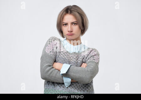 Beautiful girl frowning her face in displeasure, wearing sweater, keeping arms folded. Attractive young woman in closed posture, because she is offend Stock Photo