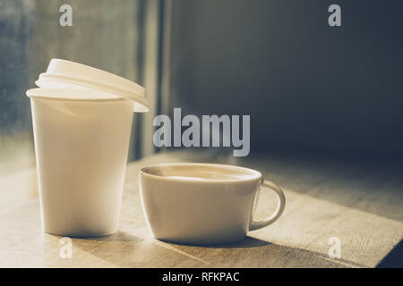 Coffee in ceramic cup and in paper cup to go on table in cafe. Horizontal Toning Stock Photo