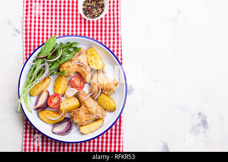 Homemade tasty roasted chicken wings with roasted potato with vegetables in an enamel bowl, top view, horizontal with place for text Stock Photo