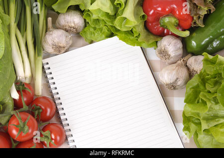 Selection of salad vegetables with lined notebook on a check tablecloth. Stock Photo